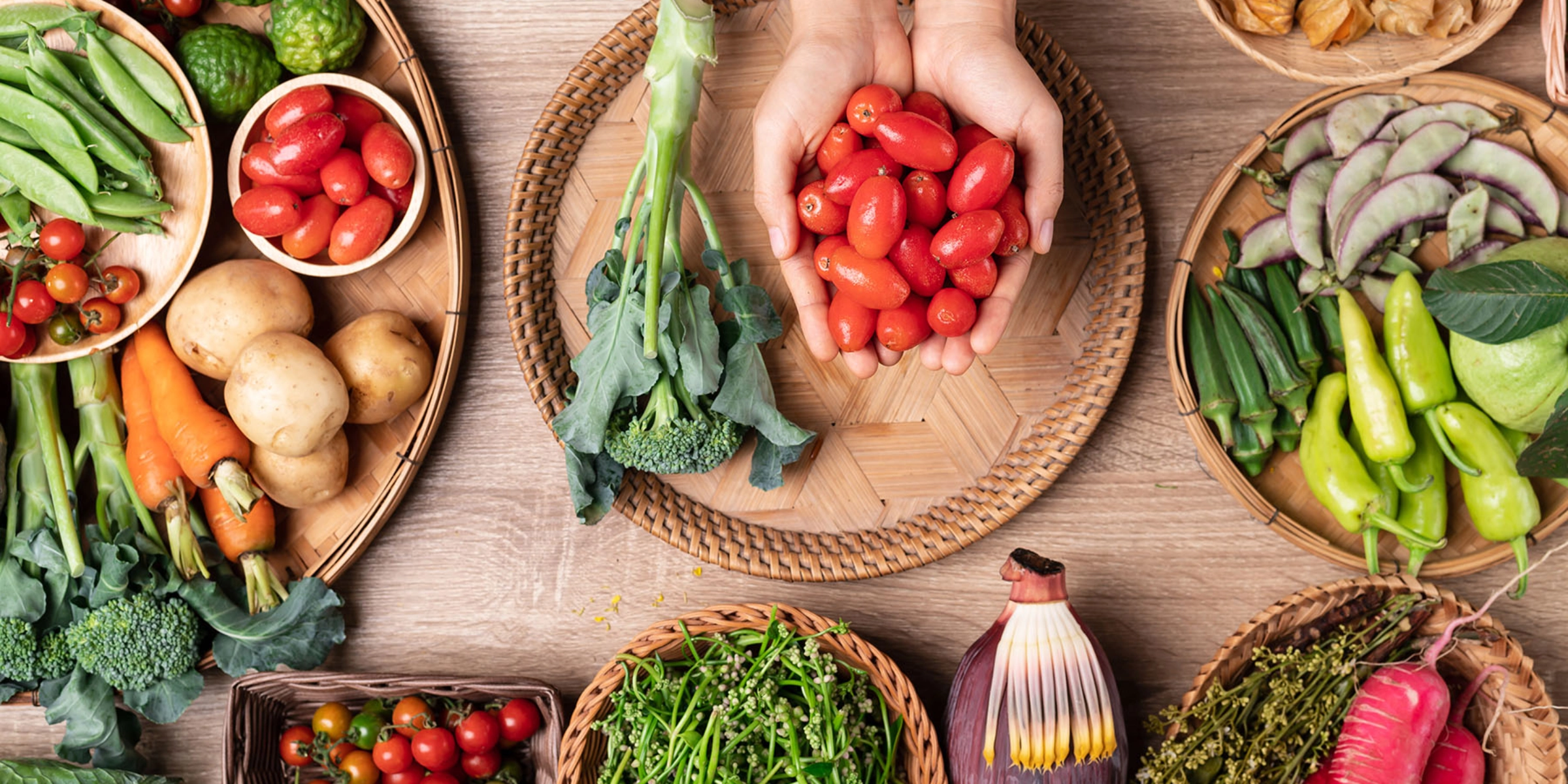 Différents légumes frais sur une table, au centre, quelqu'un tient des tomates cerises dans ses mains.