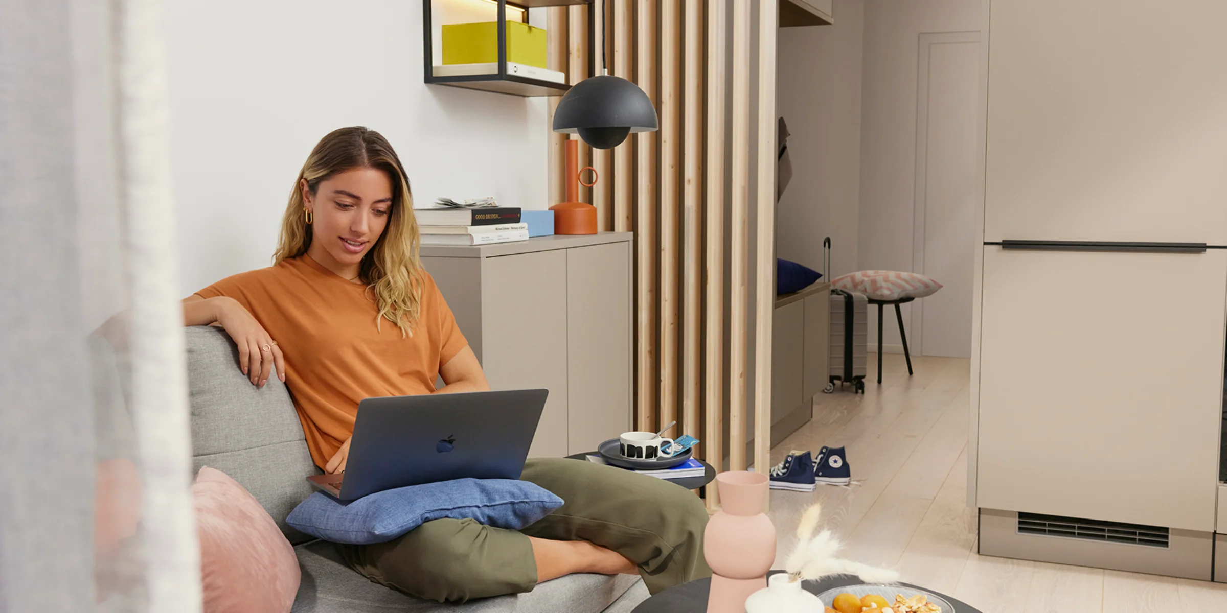 Een vrouw zit in een modern ingerichte woonkamer op een bank met een laptop, omringd door stijlvolle decoraties van Nolte Living.