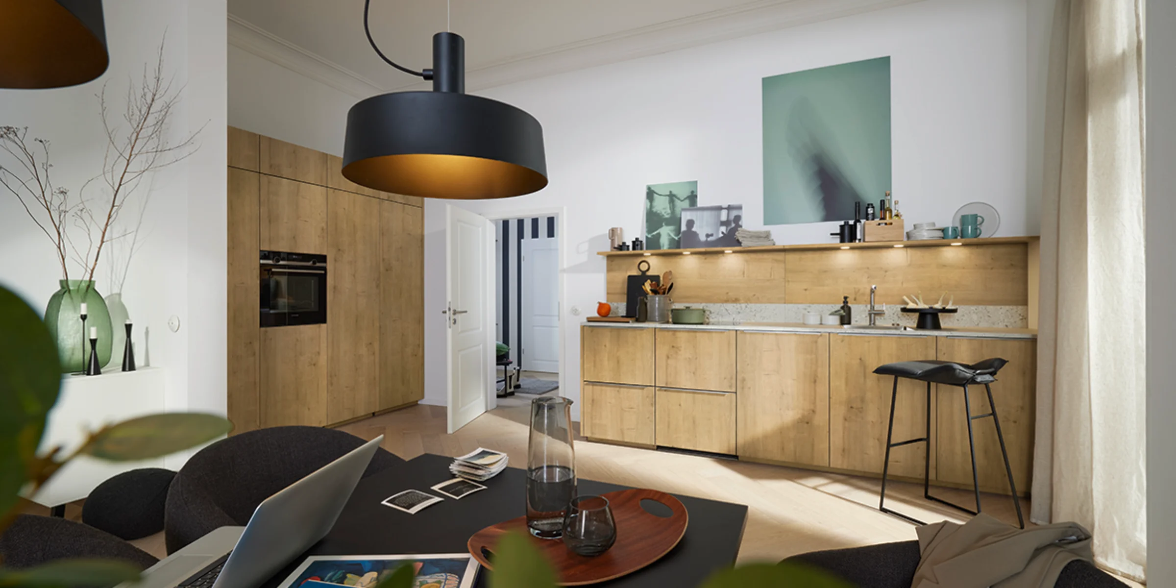 A modern kitchen with wood fronts and stylish lighting, dining table in the foreground. Nolte Kitchens.