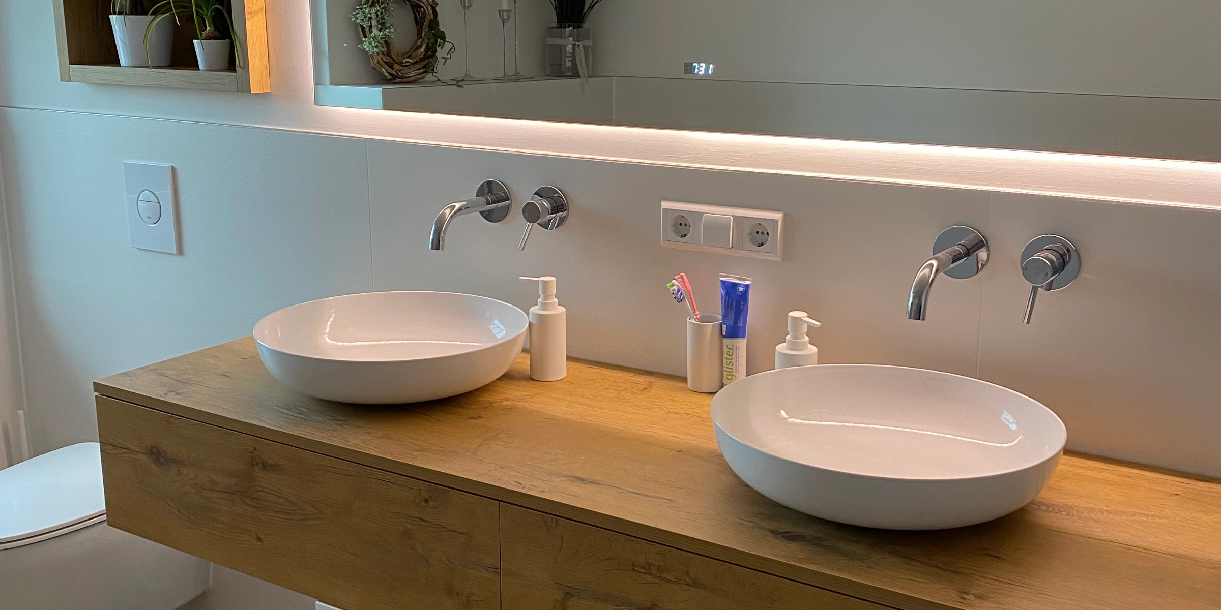 Une salle de bain moderne avec double vasque et miroir, décorée de plantes. Nolte SPA.