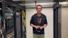 Ein Mann steht in einem Serverraum zwischen Regalen mit Kabeln und Technik.