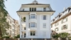 Ein weißes Mehrfamilienhaus mit mehreren Balkonen und einem Garten davor.