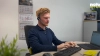 Ein Mann arbeitet konzentriert an einem Schreibtisch mit Computer und Headset; im Hintergrund das Logo von Nolte Küchen.