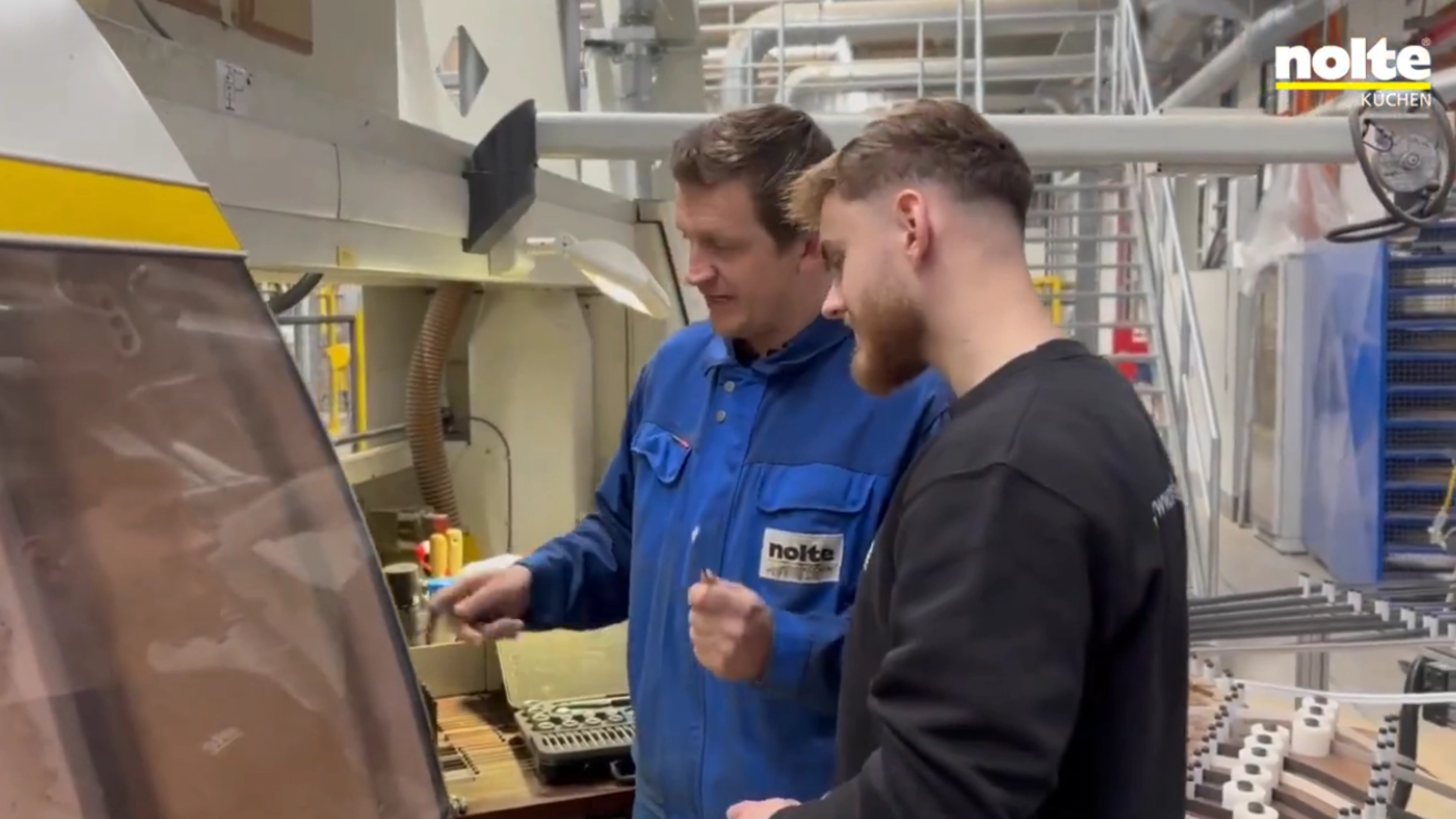 Zwei Männer arbeiten in einer Fabrik an einer Maschine, Nolte Küchen.
