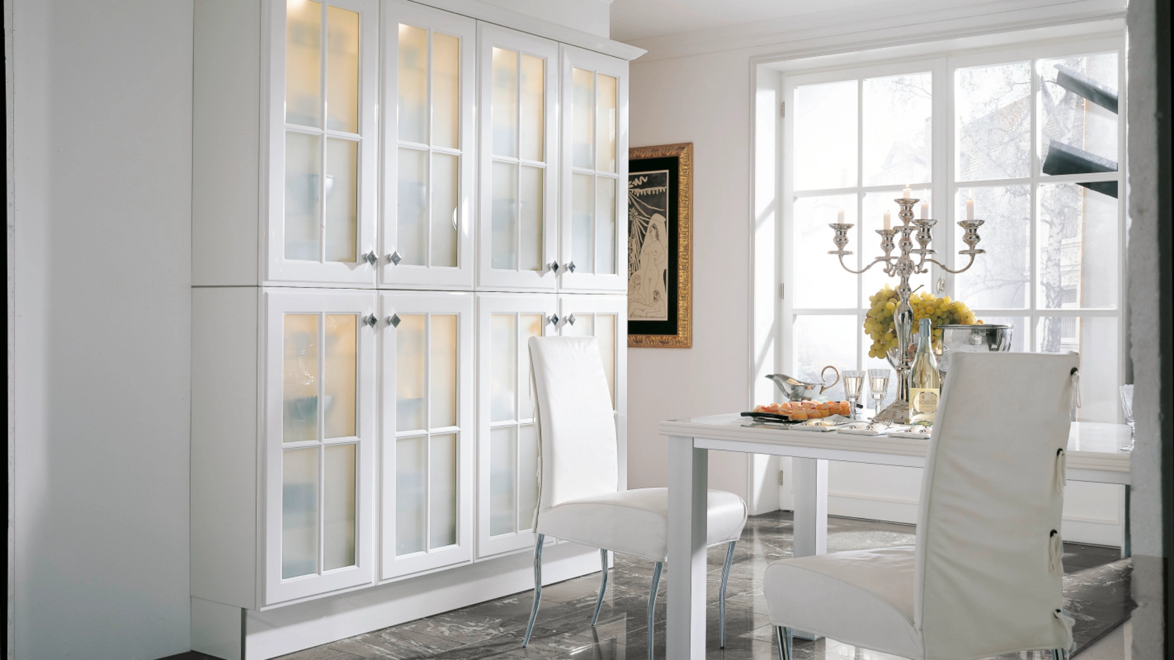 A stylish dining area with white furniture and glass doors exudes elegance, complemented by Nolte Living.