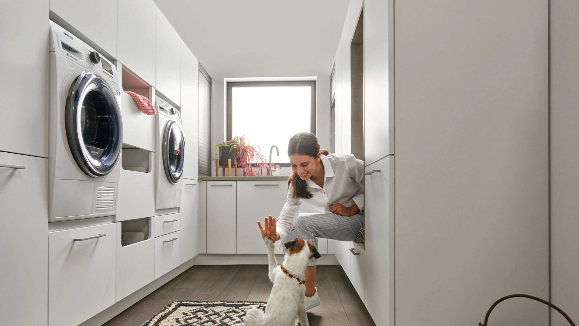 Une femme joue avec un chien dans une buanderie moderne de Nolte Utility Rooms.