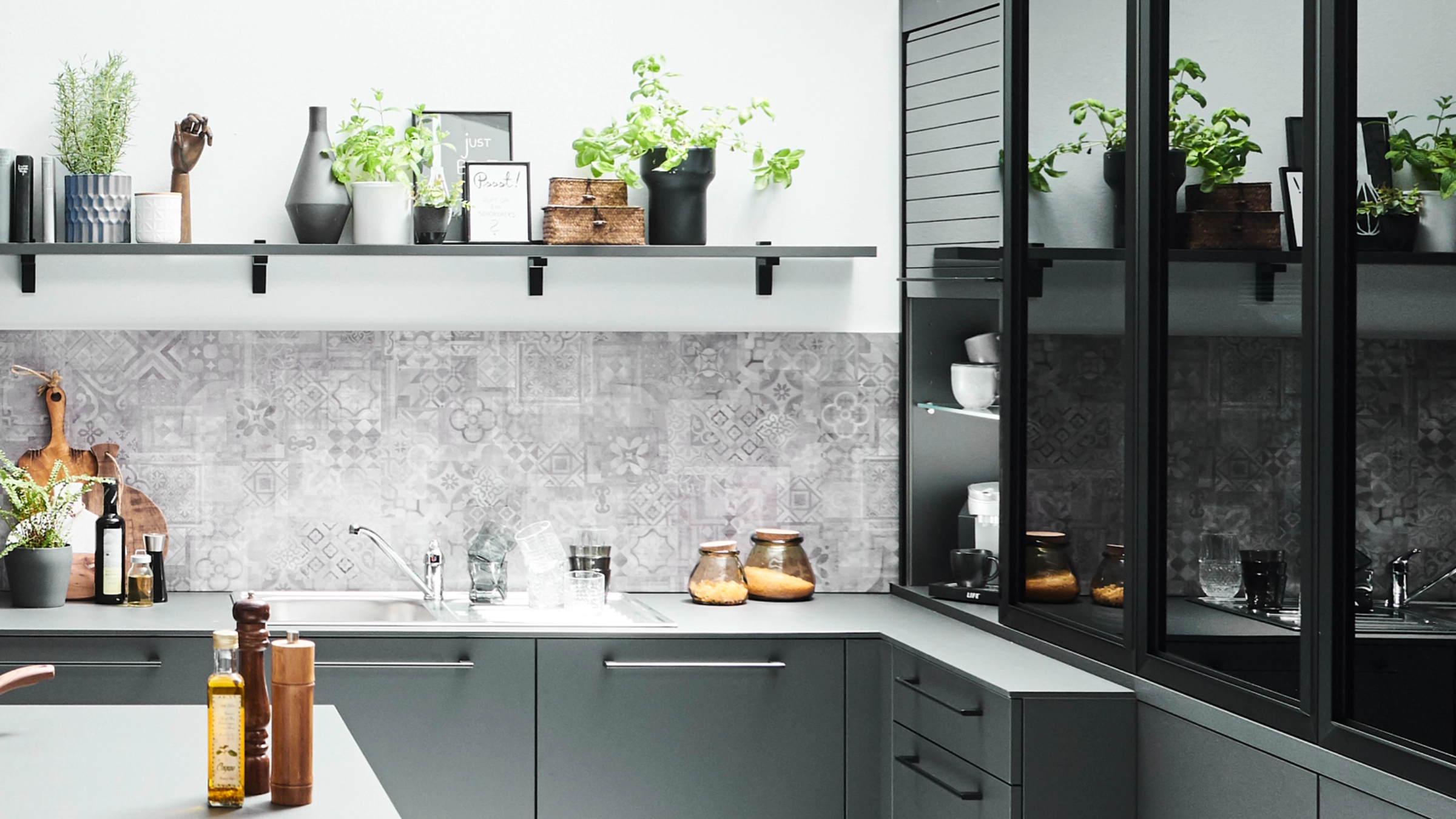 Modern gray kitchen with plants and decorative tiles in the background, designed by Nolte Kitchen.