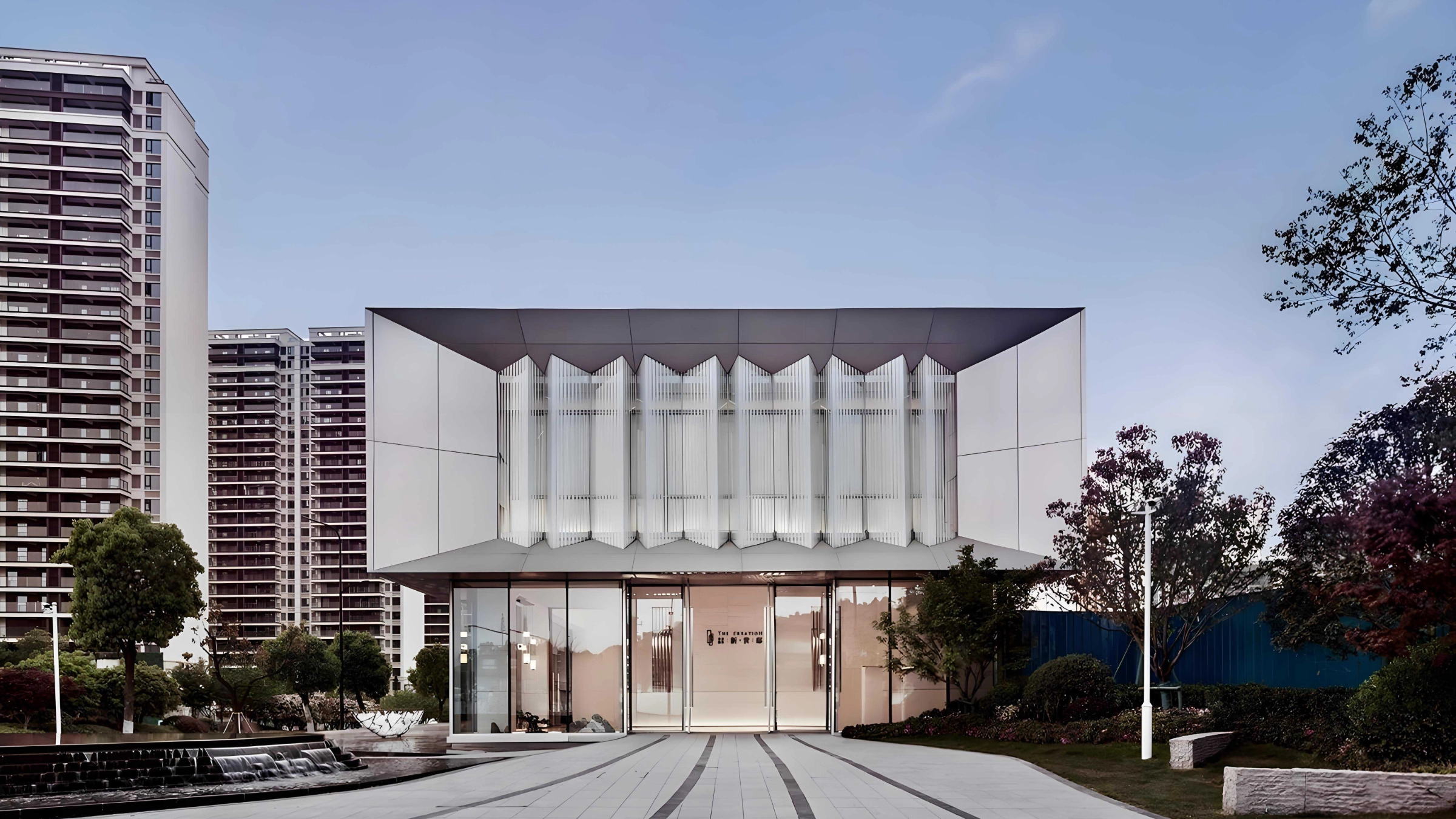 Ein modernes Gebäude mit Glasfront und umliegender Gartenlandschaft bei Tageslicht.
