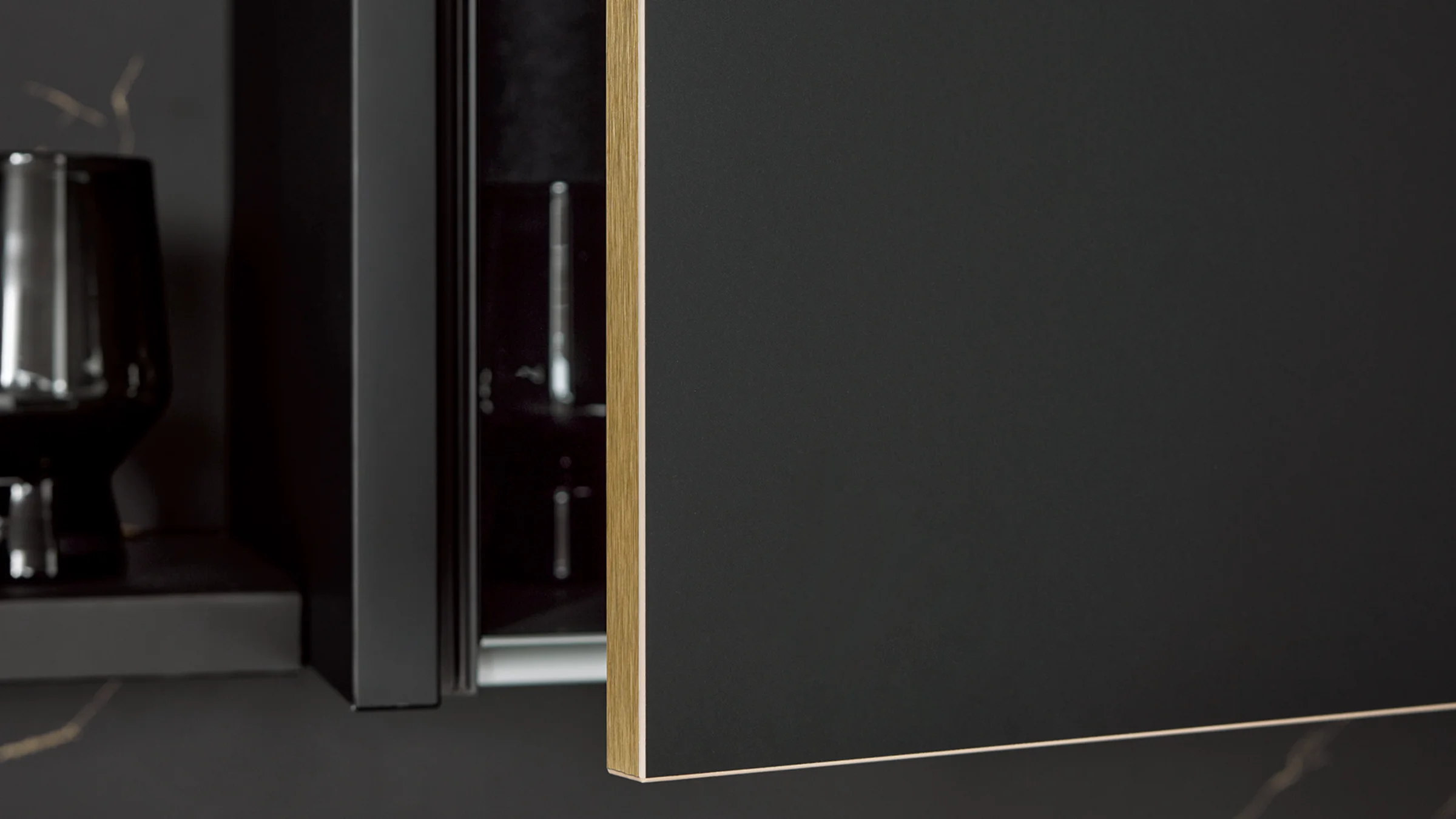 Moderne nolte Küchen Front FLAIR in Schwarz softmatt mit eleganter Messingkante, kombiniert mit warm beleuchtetem Rückwandpaneel und dunkler Arbeitsplatte.