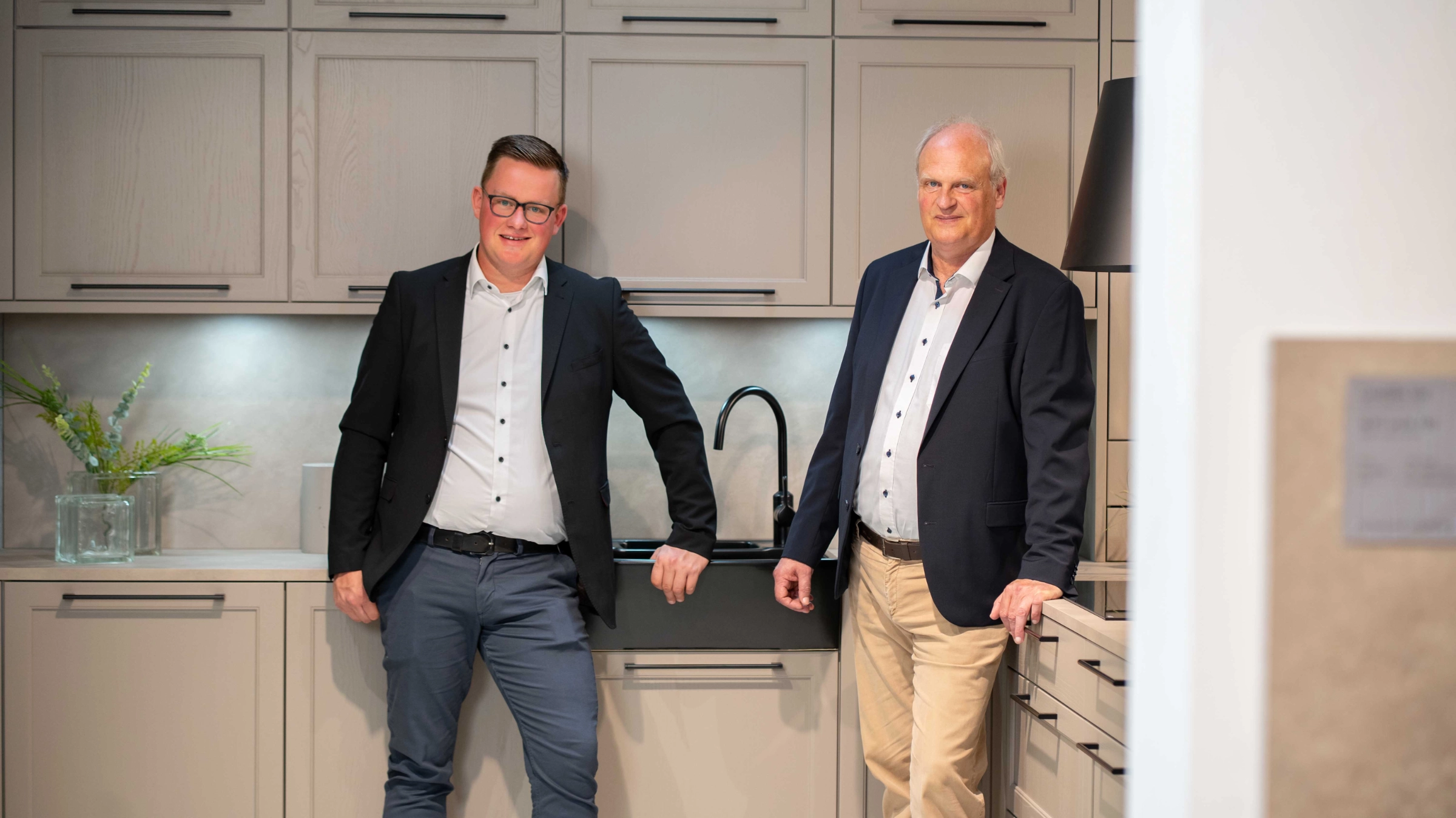 Deux hommes dans une cuisine moderne avec placards beiges et robinet noir. Nolte Kitchen.