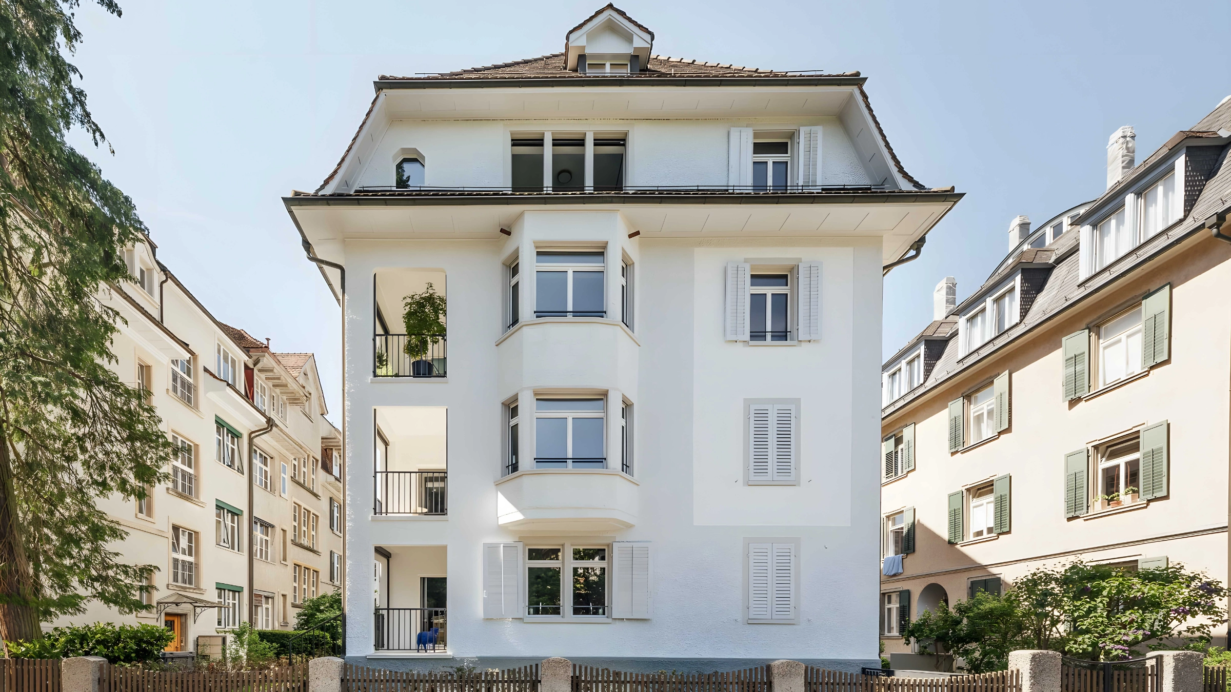 Ein weißes Mehrfamilienhaus mit mehreren Balkonen und einem Garten davor.