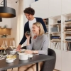 Un couple savoure un repas dans un espace moderne avec bibliothèque et cuisine, Nolte Living.