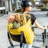 Persoon duwt een fiets en draagt een grote gele tas vol met boodschappen.