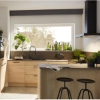 Cuisine moderne avec armoires en bois et plantes, éclairée par une grande fenêtre. Nolte Kitchen.