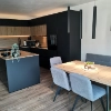 Cuisine moderne avec accents bois et noirs, table à manger et chaises, conçue par Nolte Kitchen.