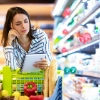 Une femme regarde pensivement une liste de courses au supermarché.
