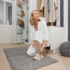 Une femme agenouillée dans un couloir élégant avec étagère à chaussures et tapis, partie de Nolte Living.