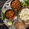 Un repas avec curry de pois, riz, pain, citron vert et épices, joliment présenté sur un plateau.