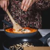 Person kocht in einer modernen Küche mit zwei Pfannen. Nolte Küchen Rezept.