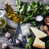 Sur une table en bois, des ingrédients pour le pesto, dont basilic, parmesan et ail.