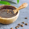Un bol avec un gommage au marc de café et des grains de café sur fond gris.