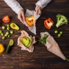 Une personne emballe des légumes dans des feuilles de cire d'abeille, y compris poivron, brocoli et avocat.