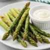 Green asparagus on a white plate with a bowl of dip.