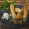 Knusprige Teigröllchen gefüllt mit Käse auf einem Schieferteller, dekoriert mit frischen Kräutern.