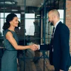 Zwei Personen in Geschäftskleidung schütteln sich die Hand in einem modernen Büro.