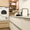 A bright utility room with a washing machine and shelves, designed by Nolte Utility Rooms.