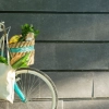 Un vélo avec un panier rempli de courses est appuyé contre un mur sombre.