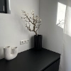 Sur le comptoir noir, un vase blanc et un vase noir avec une branche, assortis à Nolte Living.