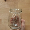 Une main tient un verre entouré d'une ficelle sur une table en bois.