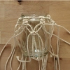 Un bocal avec support en macramé sur une table en bois.