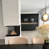 A modern kitchen with black decor and a fireplace, dining table in the foreground. Nolte Kitchens.