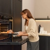 Une femme sort un pain fraîchement cuit du four dans une cuisine moderne de Nolte Kitchen.