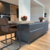 Cucina moderna con isola scura e ciotola di frutta su bancone in legno, sullo sfondo cucine Nolte.