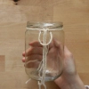Une main noue une corde autour d'un bocal vide.