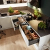 Une cuisine moderne avec tiroirs ouverts et herbes fraîches sur le plan de travail. Nolte Kitchen.