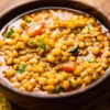 Un bol en bois rempli de ragoût de lentilles jaunes, garni d'herbes fraîches et de morceaux de carottes.