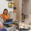Une femme est assise dans un salon moderne sur un canapé avec un ordinateur portable, entourée de décorations Nolte Living.