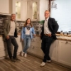 Tres personas en una cocina moderna con pared de piedra y suelo de madera. Nolte Cocina.