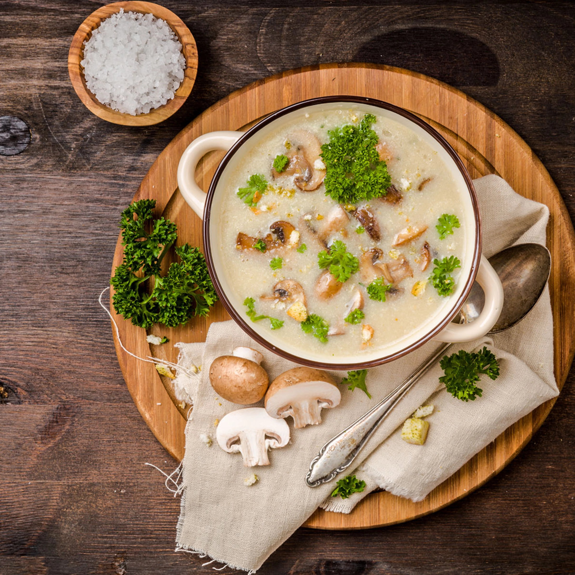 Une assiette de soupe aux champignons avec du persil et des champignons frais sur une table en bois.
