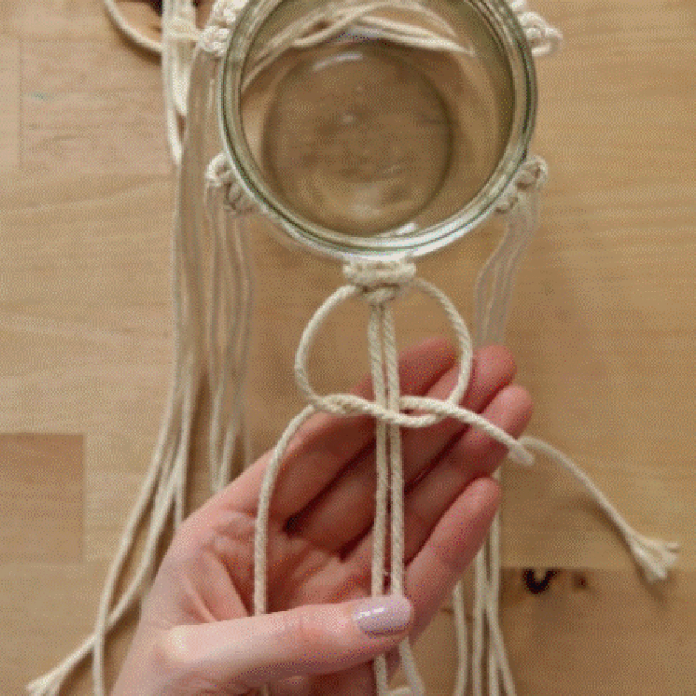 Une personne fait du macramé autour d'un bocal en verre.