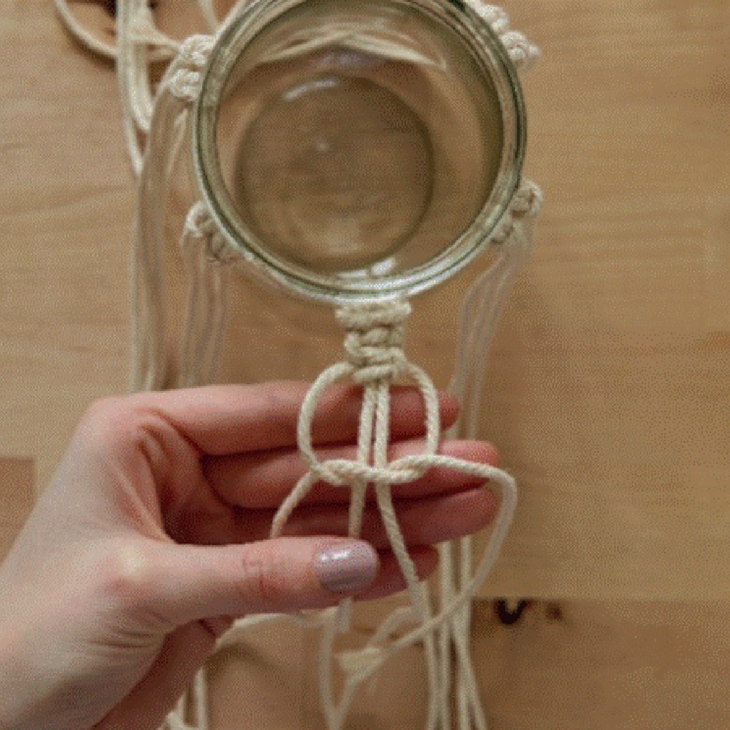 Une main noue des cordons de macramé autour d'un bocal en verre.