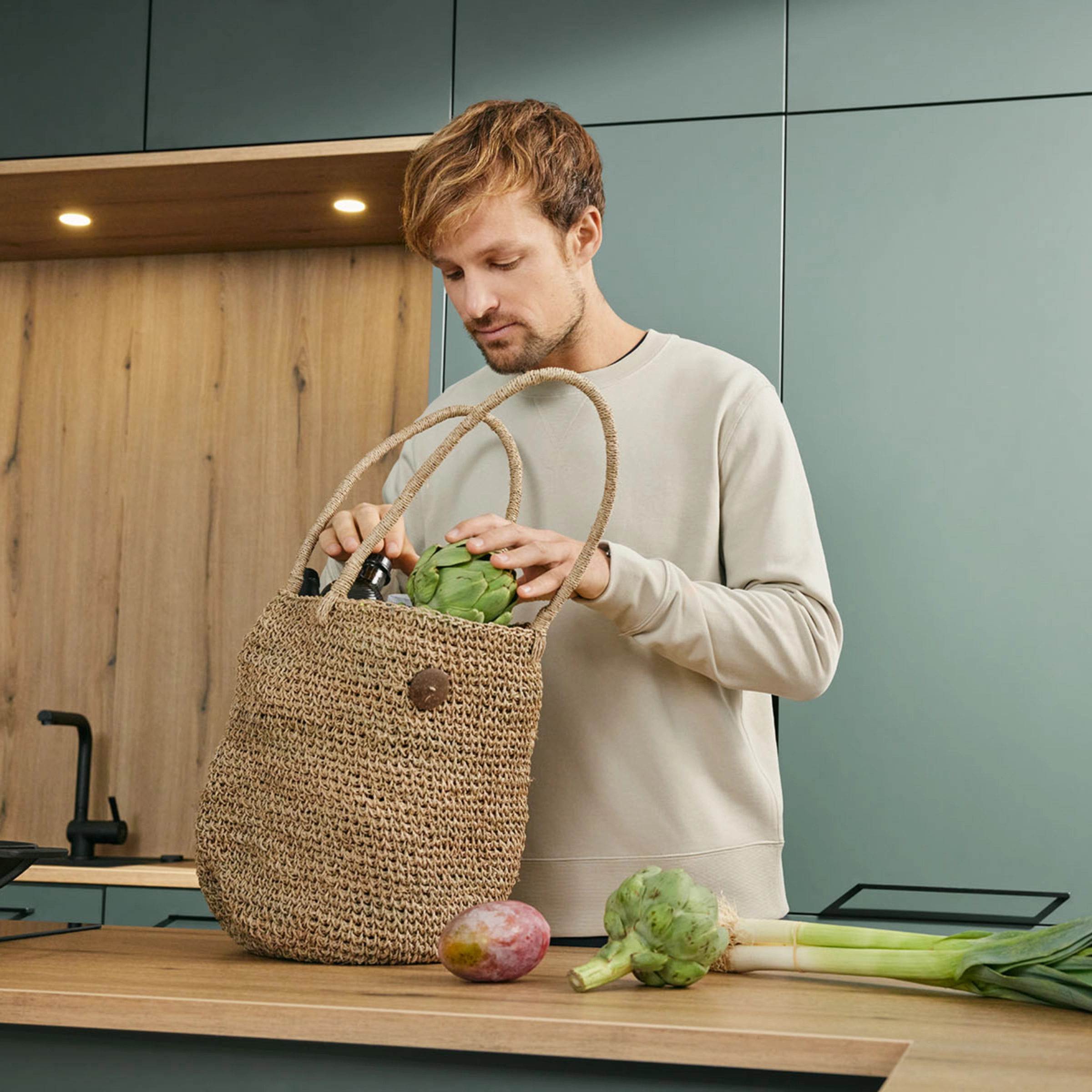 Een man staat in een moderne Nolte-keuken en legt boodschappen uit een juten tas op het aanrecht.