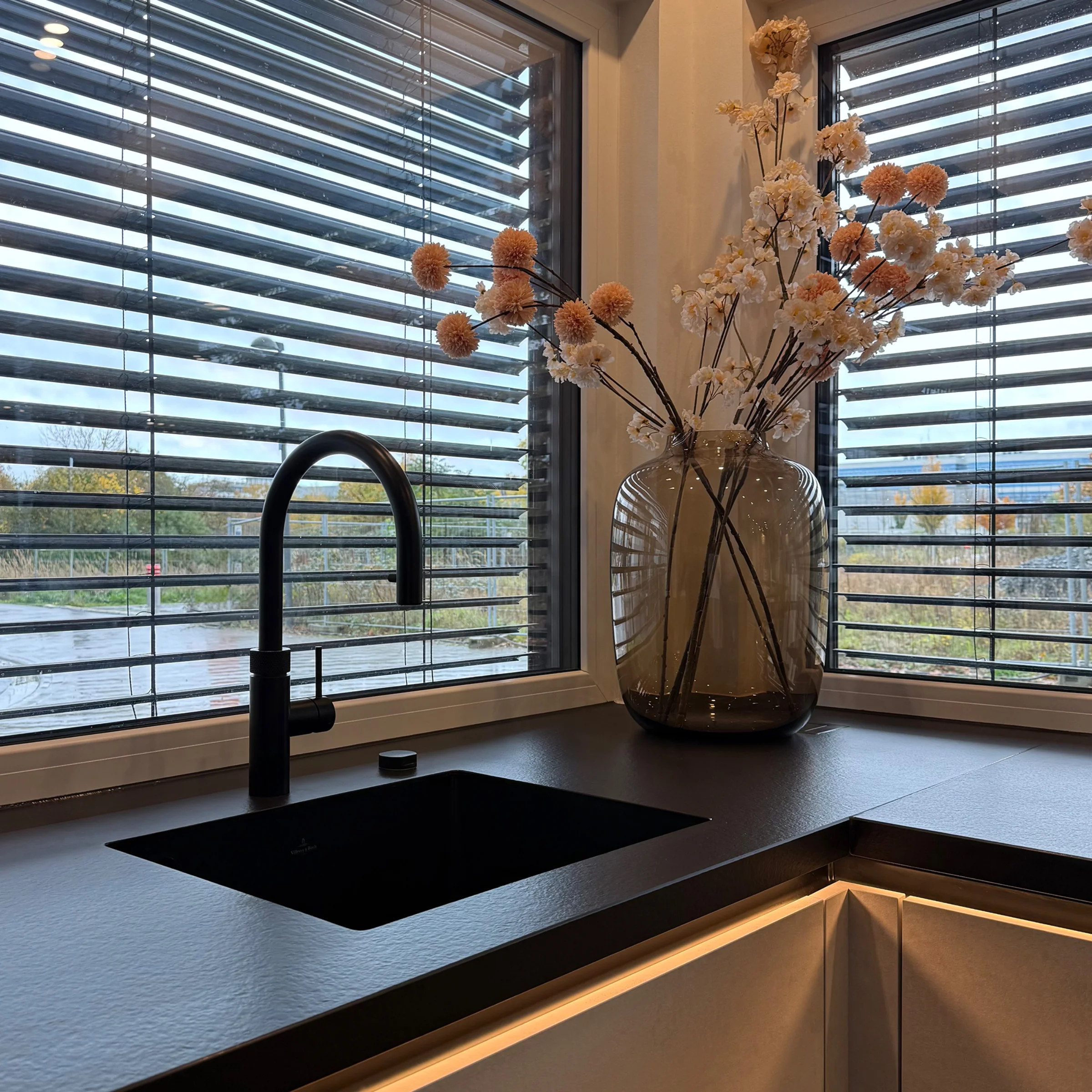 Eine moderne Küche mit schwarzem Wasserhahn und großen Fenstern. Nolte Küchen.