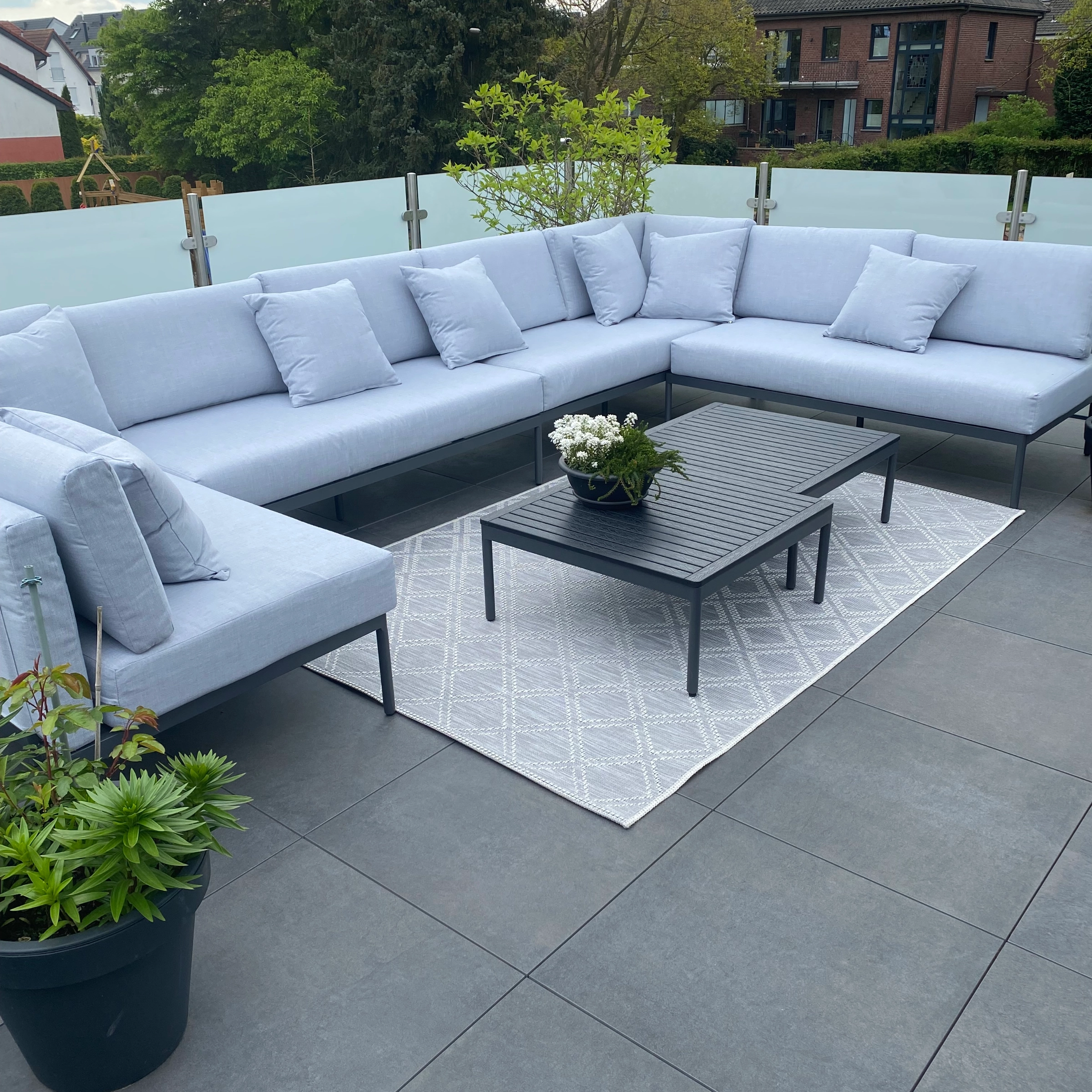 Une terrasse moderne avec canapé gris et table, entourée de plantes.