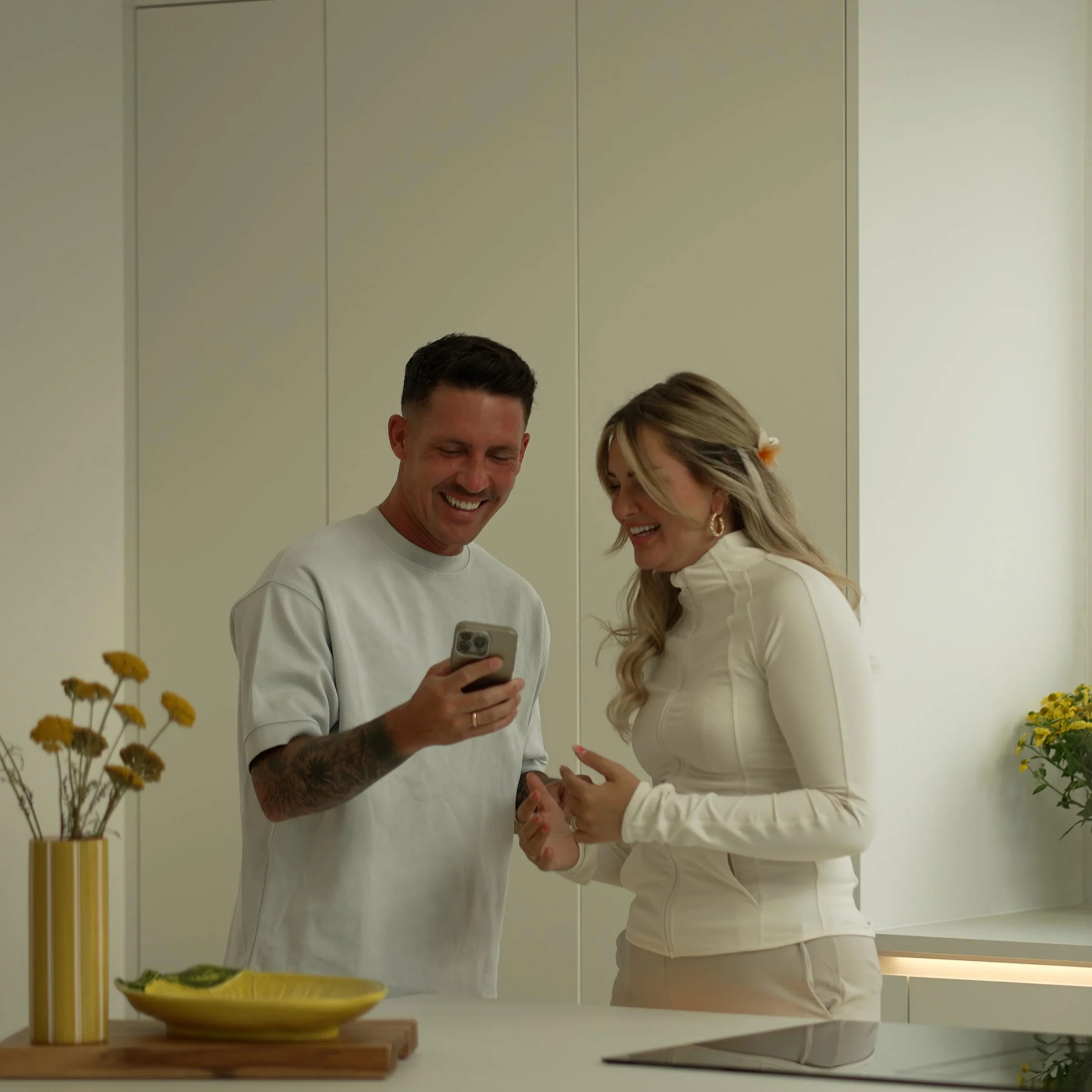 Une cuisine moderne avec deux personnes souriantes, des plantes et une assiette jaune. Nolte Küchen.