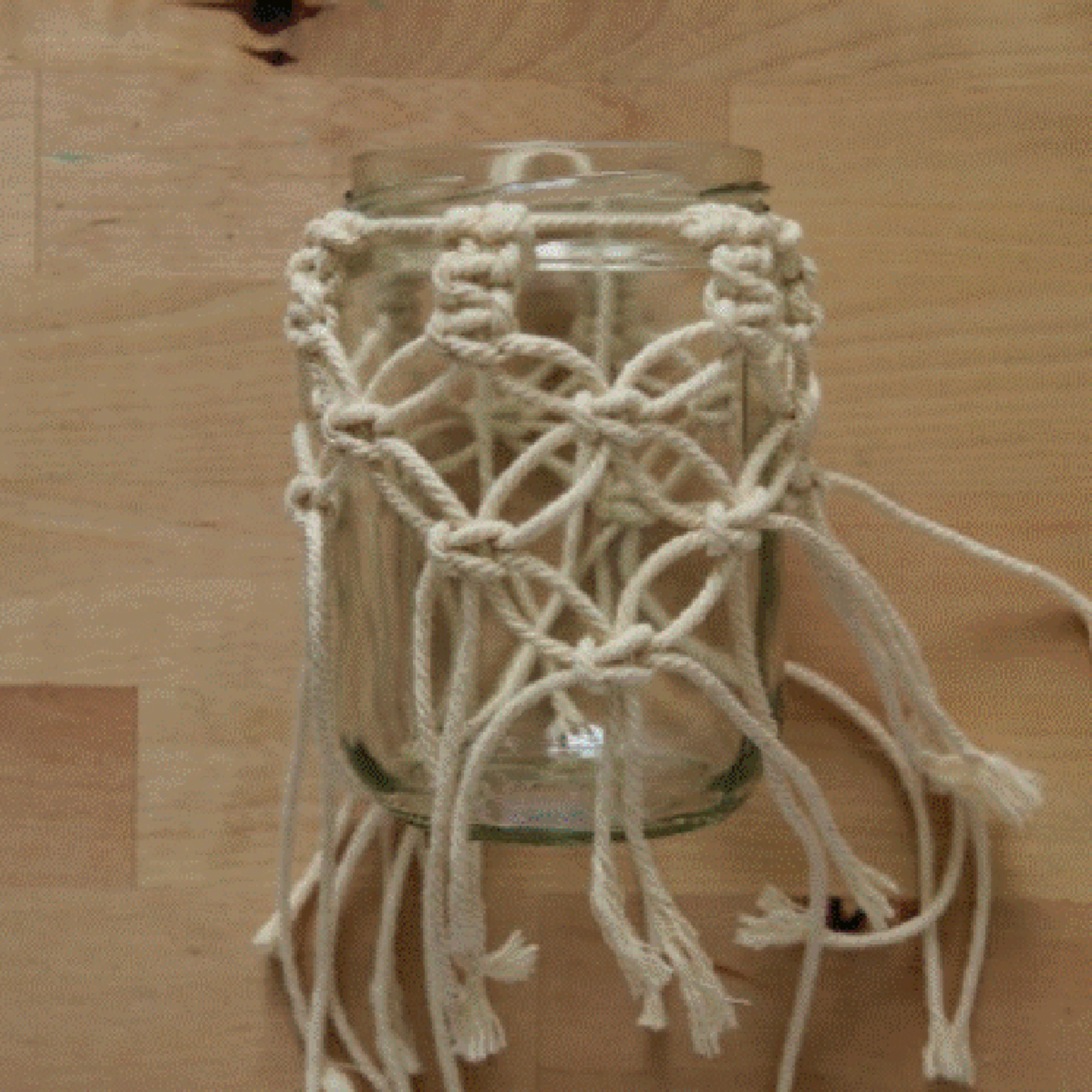 Un verre avec décoration macramé sur une table en bois.